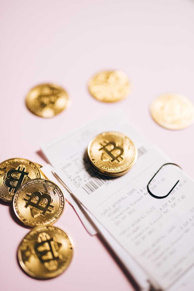 Close-up of Bitcoin coins and financial receipts on a pink background.